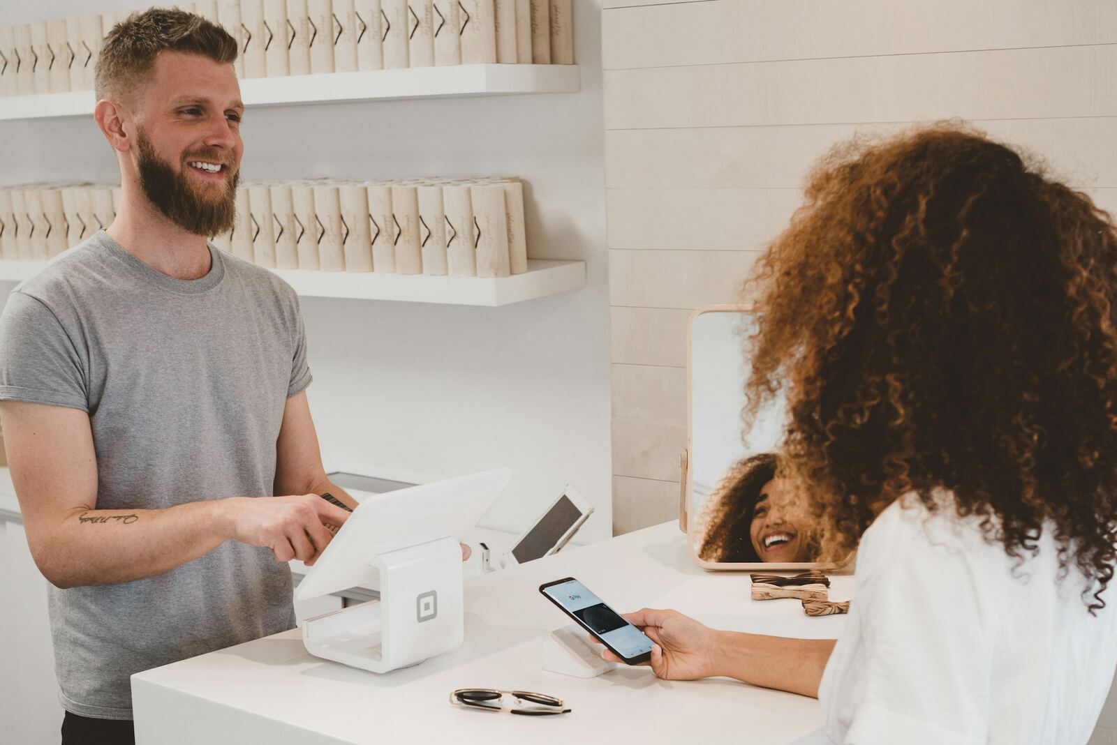 A small-business owner laughing with a customer paying by phone at the counter